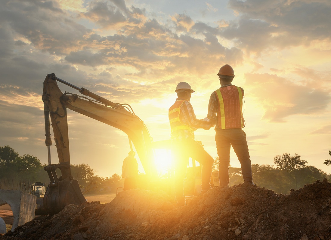 Insurance by Industry - Rear View of Two Contractors Standing on a Pile of Excavated Dirt on a Construction Jobsite at Sunset with a Colorful Sky