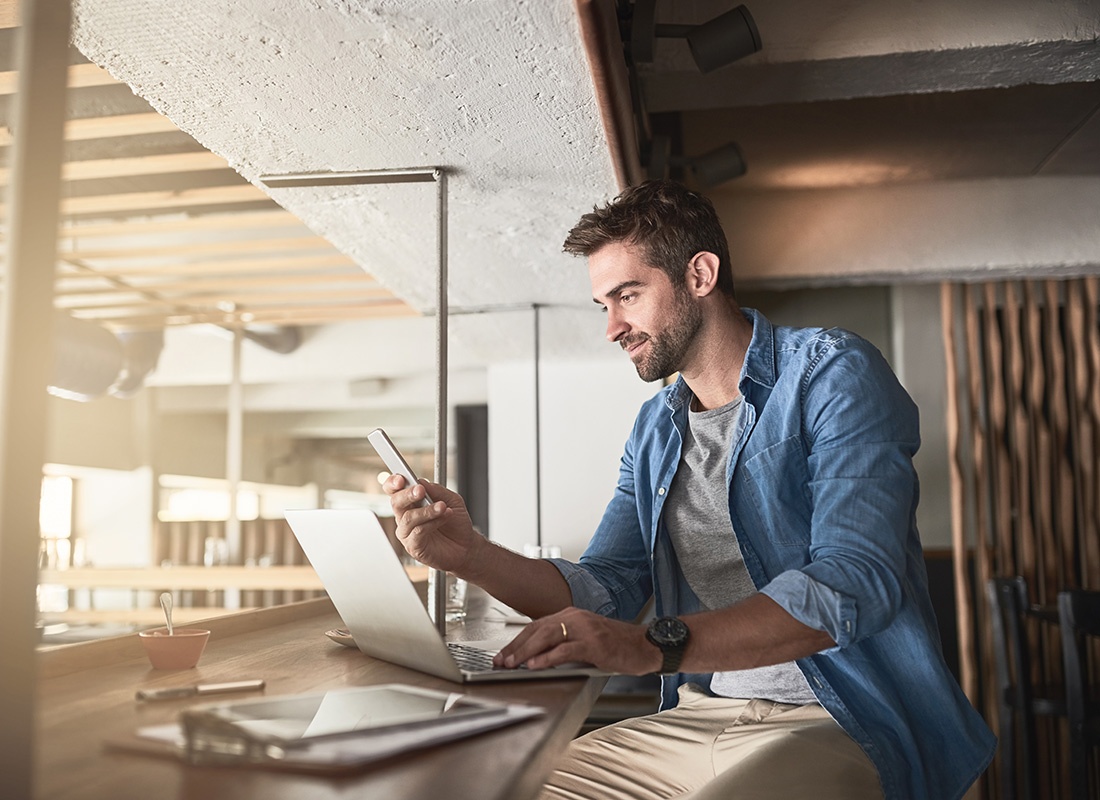 Read Our Reviews - View of a Young Business Owner Sitting Inside a Modern Restaurant While Working on a Laptop and Holding a Phone in his Hands