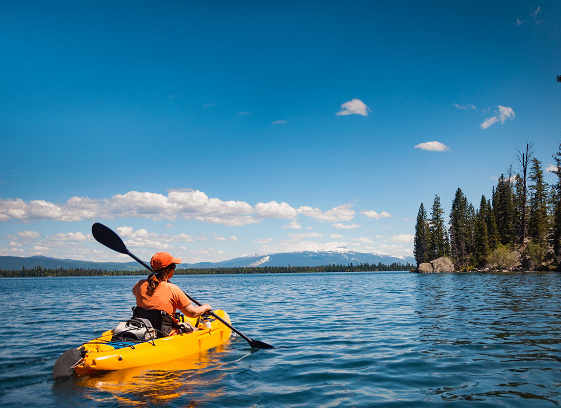 We Are Independent - Rear View of a Young Woman on a Kayak on a Lake Surrounded by Evergreen Trees in a State Park in Wyoming on a Sunny Day